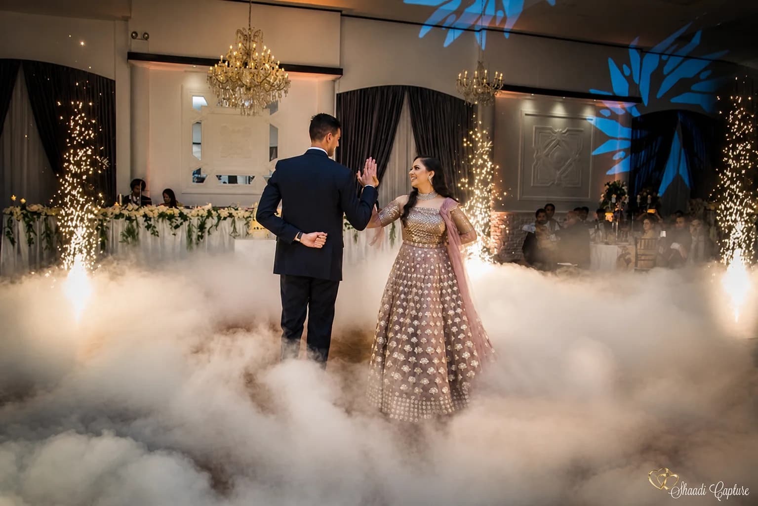 Newlyweds sharing a first dance through low-lying clouds and spark fountains
